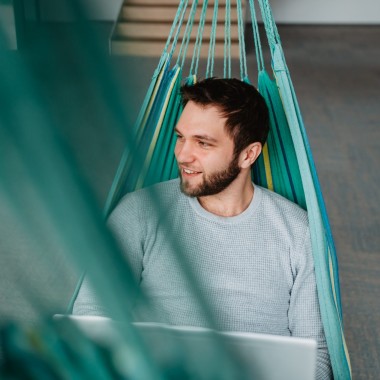 muž leží na houpací síti a pracuje na notebooku